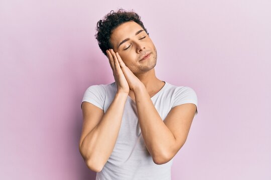 Young handsome man wearing casual white t shirt sleeping tired dreaming and posing with hands together while smiling with closed eyes.