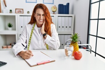 Young redhead woman nutritionist doctor at the clinic touching mouth with hand with painful...