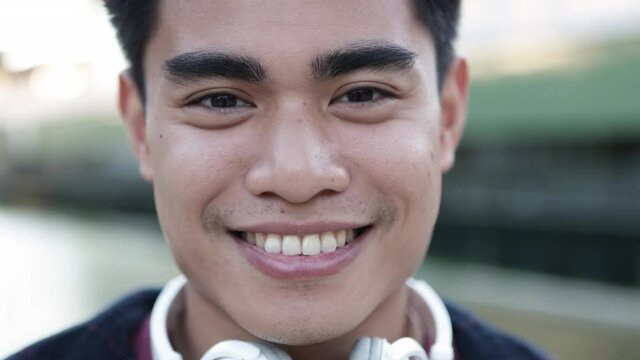 Closeup portrait of handsome young asian man with headphones smiling at camera - Millennial people concept. High quality 4k footage