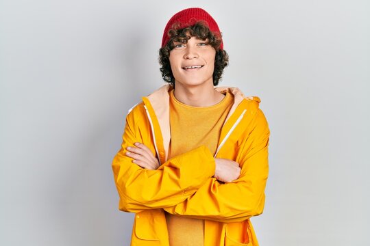 Handsome young man wearing yellow raincoat happy face smiling with crossed arms looking at the camera. positive person.
