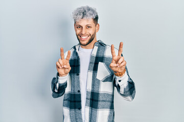 Naklejka premium Young hispanic man with modern dyed hair wearing casual shirt smiling looking to the camera showing fingers doing victory sign. number two.