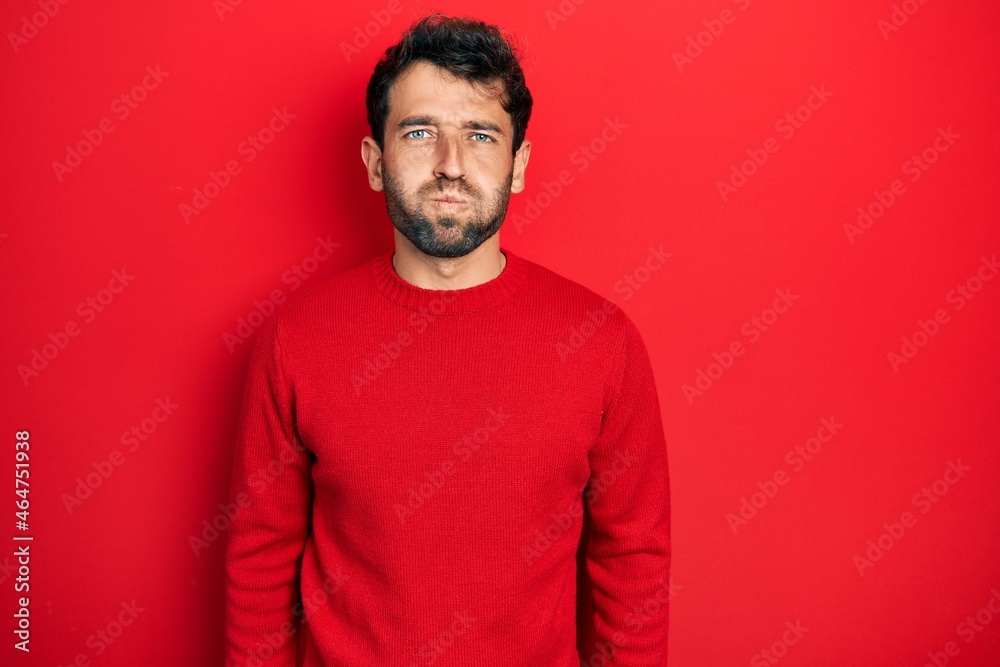 Poster handsome man with beard wearing casual red sweater puffing cheeks with funny face. mouth inflated wi