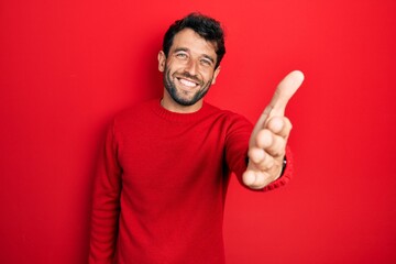 Naklejka premium Handsome man with beard wearing casual red sweater smiling friendly offering handshake as greeting and welcoming. successful business.