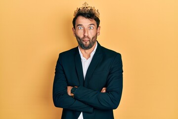 Handsome man with beard wearing business suit with arms crossed gesture and king crown making fish...