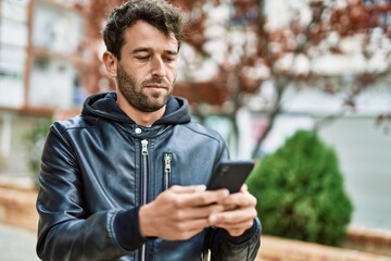 Fototapeta premium Handsome hispanic man with beard with serious face outdoors using smartphone