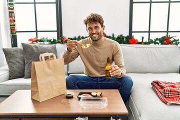 Young hispanic man eating take away sushi sitting by christmas decor at home