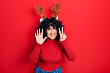 Young middle east woman wearing cute christmas reindeer horns showing and pointing up with fingers number seven while smiling confident and happy.