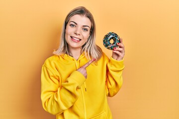 Beautiful caucasian woman holding donut smiling happy pointing with hand and finger