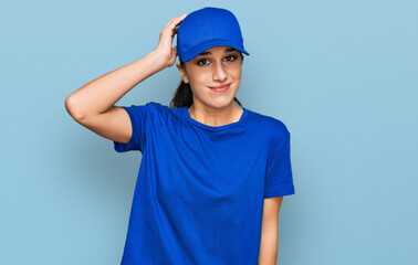 Young hispanic girl wearing delivery courier uniform confuse and wonder about question. uncertain...