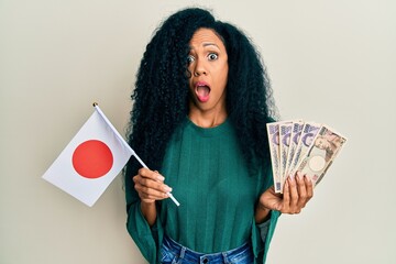 Middle age african american woman holding japan flag and yen banknotes afraid and shocked with surprise and amazed expression, fear and excited face.