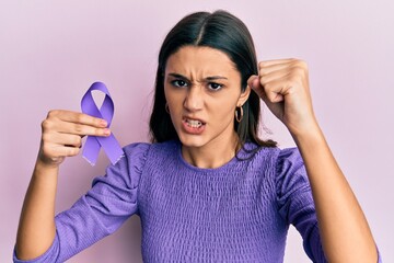 Young hispanic woman holding purple ribbon awareness annoyed and frustrated shouting with anger,...