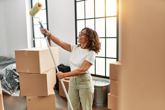 Middle age hispanic woman smiling confident holding paint roller at new home