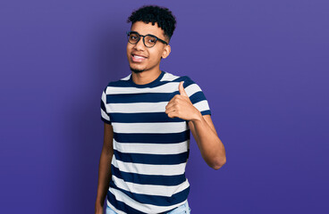 Young african american man wearing casual clothes and glasses doing happy thumbs up gesture with hand. approving expression looking at the camera showing success.