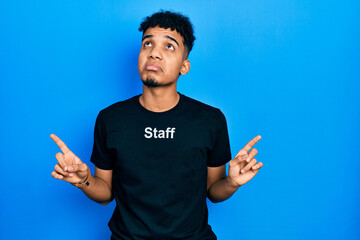 Young african american man wearing staff t shirt pointing up looking sad and upset, indicating...