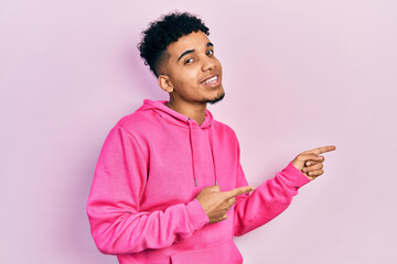 Young african american man wearing casual sweatshirt smiling and looking at the camera pointing with two hands and fingers to the side.