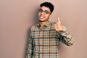 Young african american man wearing casual clothes and glasses smiling happy and positive, thumb up doing excellent and approval sign