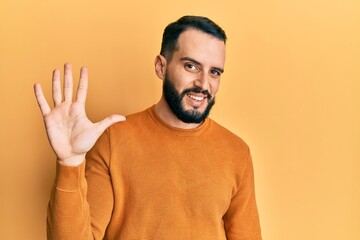 Young man with beard wearing casual winter sweater showing and pointing up with fingers number five while smiling confident and happy.