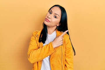 Beautiful hispanic woman with nose piercing wearing yellow leather jacket pointing with hand finger to the side showing advertisement, serious and calm face