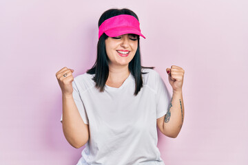 Fototapeta na wymiar Young hispanic woman wearing sportswear and sun visor cap very happy and excited doing winner gesture with arms raised, smiling and screaming for success. celebration concept.