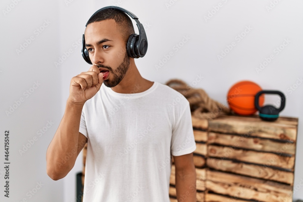 Poster African american man listening to music using headphones at the gym feeling unwell and coughing as symptom for cold or bronchitis. health care concept.