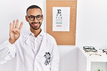 Fototapeta na wymiar African american optician man standing by eyesight test showing and pointing up with fingers number four while smiling confident and happy.