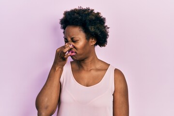 Young african american woman wearing casual sleeveless t shirt smelling something stinky and...