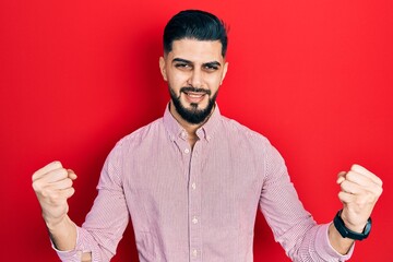 Handsome man with beard wearing casual red shirt screaming proud, celebrating victory and success...