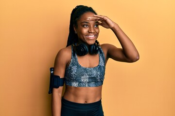 African american woman with braided hair wearing sportswear and arm band very happy and smiling looking far away with hand over head. searching concept.