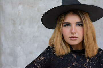 Happy gothic young woman in Halloween witch costume with hat on gray background