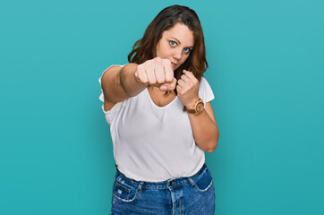 Young plus size woman wearing casual white t shirt punching fist to fight, aggressive and angry attack, threat and violence