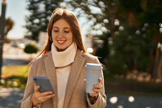 Young redhead girl using smartphone drinking coffee at the city.