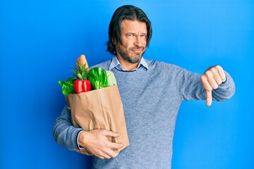 Middle age handsome man holding paper bag with groceries with angry face, negative sign showing dislike with thumbs down, rejection concept