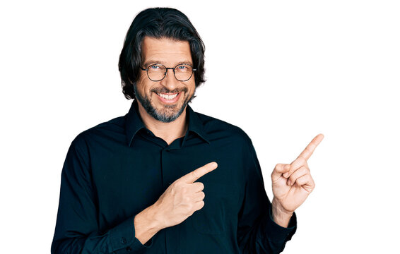 Middle age caucasian man wearing casual clothes and glasses smiling and looking at the camera pointing with two hands and fingers to the side.