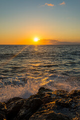 romantic sunset on the mediterranean coast with bursts of sea waves in the sun