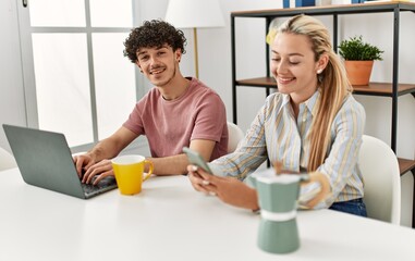 Young couple using laptop and smartphone drinking coffee at home.