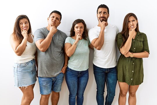 Group of young hispanic friends standing together over isolated background thinking worried about a question, concerned and nervous with hand on chin
