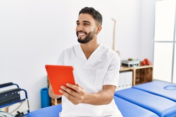 Young arab man wearing physiotherapist uniform using touchpad at clinic