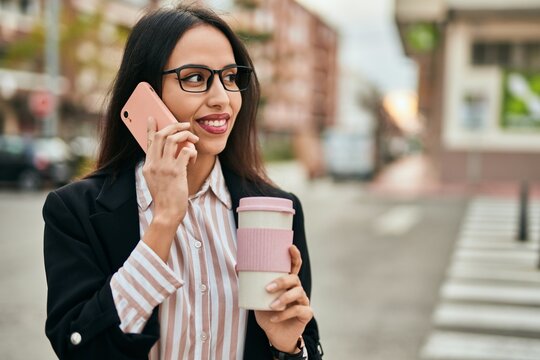 Young hispanic businesswoman talking on the smartphone and drinking coffee at the city.