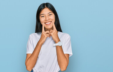 Beautiful young asian woman wearing casual white t shirt smiling with open mouth, fingers pointing and forcing cheerful smile