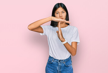 Beautiful young asian woman wearing casual white t shirt doing time out gesture with hands, frustrated and serious face