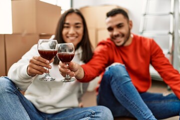 Young latin couple smiling happy toasting with red wine at new home
