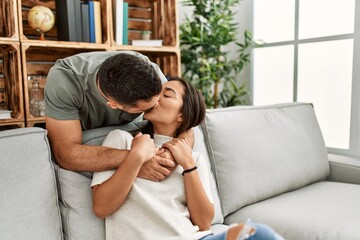 Young latin couple sitting on the sofa hugging and kissing at home.