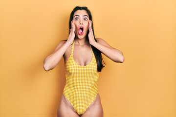 Young hispanic girl wearing swimsuit afraid and shocked, surprise and amazed expression with hands on face