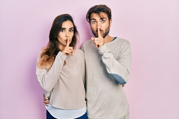 Young hispanic couple wearing casual clothes asking to be quiet with finger on lips. silence and secret concept.