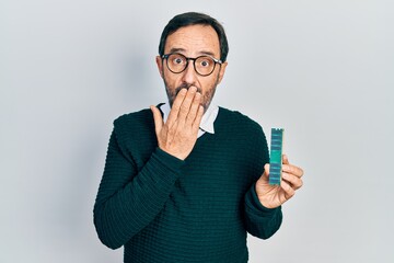 Middle age hispanic man holding memory ram covering mouth with hand, shocked and afraid for mistake. surprised expression