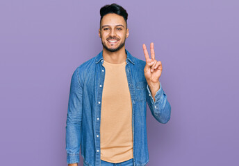 Young arab man wearing casual clothes smiling with happy face winking at the camera doing victory...