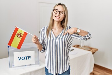Asian young woman at political campaign election holding spain flag pointing finger to one self smiling happy and proud