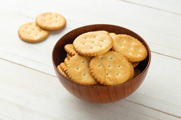 Rounded cracker cookies in a wooden bowl on white wooden table background.