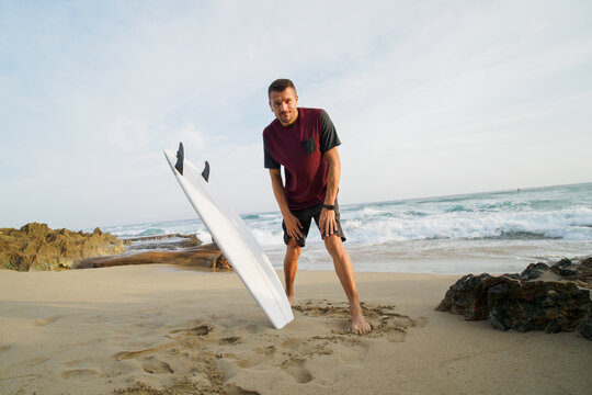 Happy man take picture with surfboard on a sandy beach next to ocean.