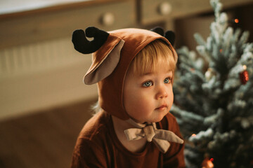 Toddler baby boy in rudolph reindeer costumes decorating Christmas tree